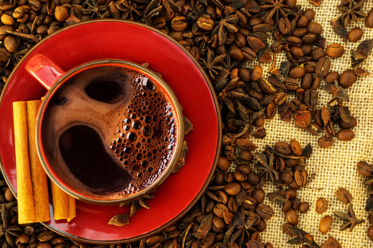 Red Cup and Saucer with Coffee and Coffee Beans on a Brown Rag Background.